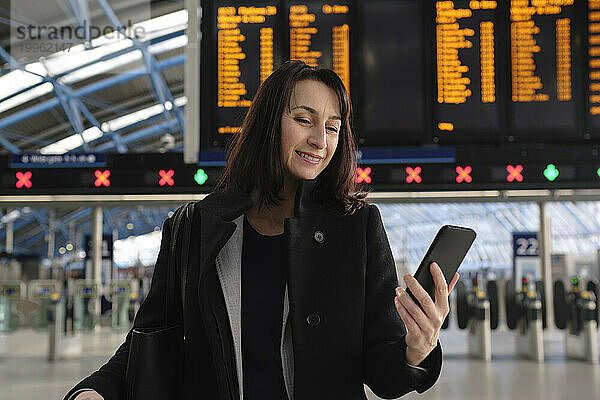 Lächelnde reife Frau  die am Bahnhof ihr Mobiltelefon benutzt