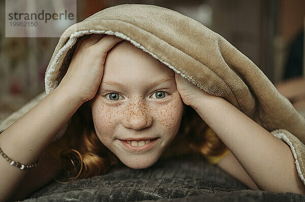 Smiling girl under blanket on bed
