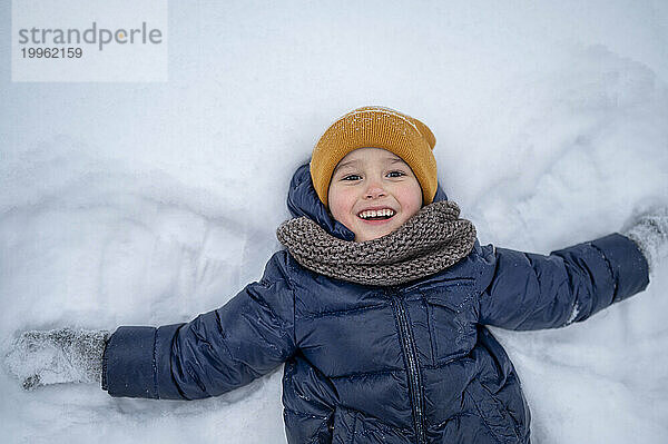Lächelnder Junge  der im Winter im Schnee liegt