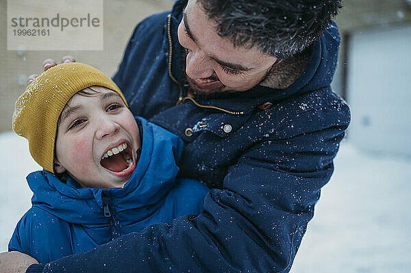 Lächelnder Vater umarmt seinen Sohn und hat Spaß mit ihm im Winter