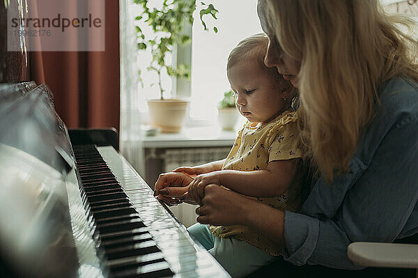 Mother teaching daughter to play piano at home