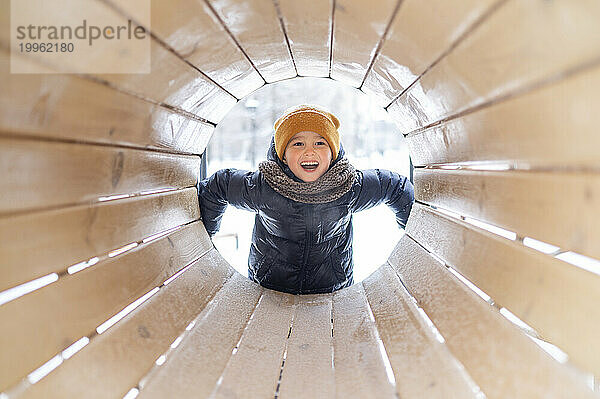 Smiling boy seen through wooden tunnel at playground