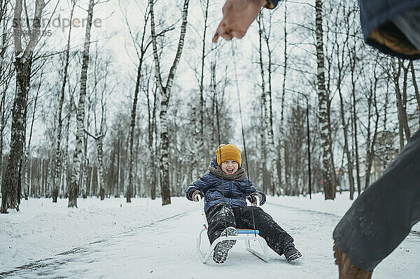 Vater rodelt glücklichen Sohn auf Schnee im Winterpark
