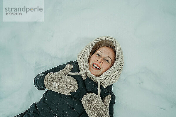 Lächelnde Frau  die im Winter auf Schnee liegt