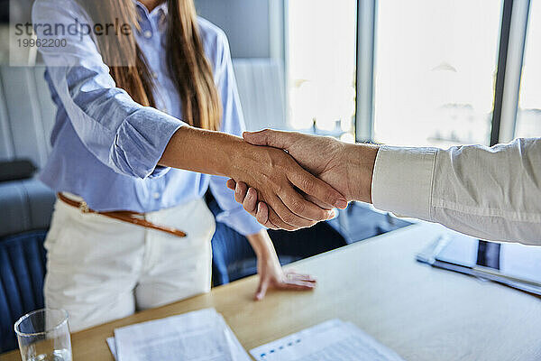 Geschäftsfrau schüttelt Geschäftsmann am Schreibtisch im Büro die Hand