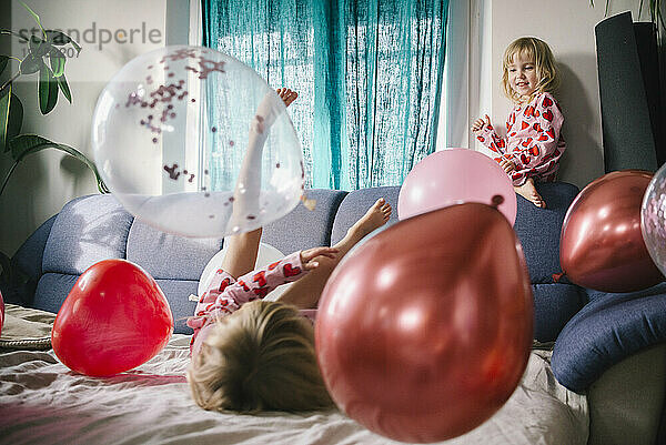 Glückliche Schwestern spielen zu Hause mit Luftballons auf dem Sofa