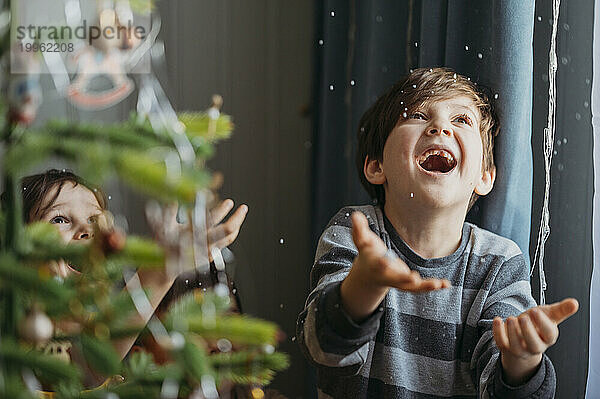 Verspielte Jungs fangen zu Hause Kunstschnee neben dem Weihnachtsbaum