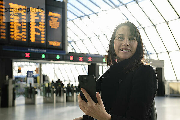Lächelnde reife Frau mit Mobiltelefon am Bahnhof