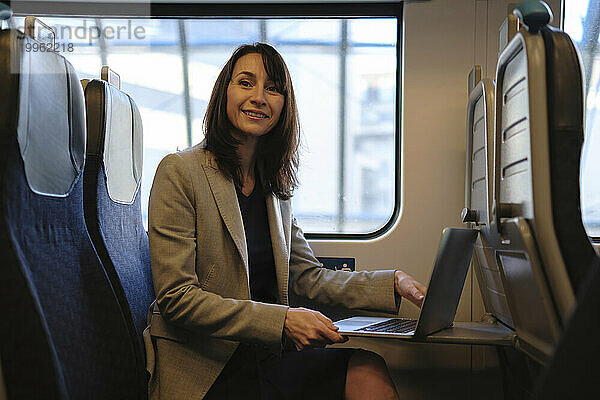 Lächelnde Geschäftsfrau sitzt mit Laptop im Zug