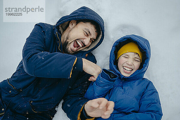 Happy father with son lying on snow and laughing in winter