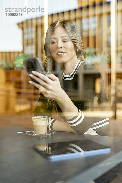 Frau sitzt und benutzt Smartphone im Café