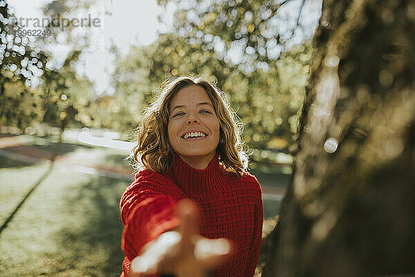 Lächelnde Frau streckt im Herbstpark die Hand aus
