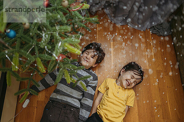 Fröhliche Brüder liegen zu Hause unter dem Weihnachtsbaum auf dem Boden
