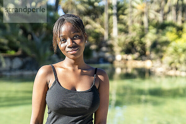 Lächelnde Frau mit schwarzem Tanktop im Park an einem sonnigen Tag