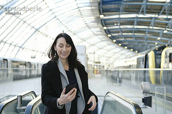 Glückliche reife Frau  die am Bahnhof ihr Smartphone benutzt