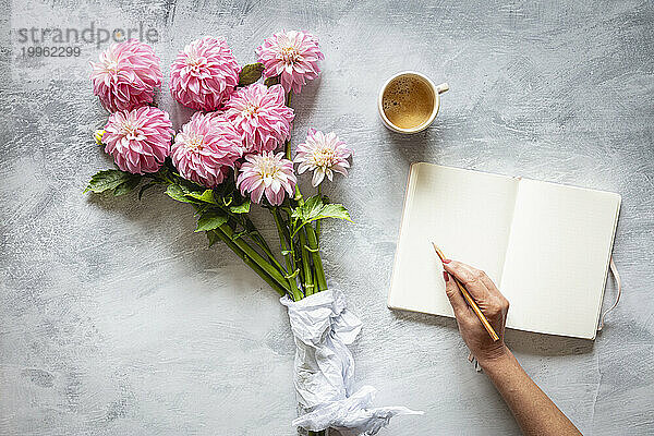 Hand of woman writing in diary in front of bouquet of pink blooming Verones DF dahlias