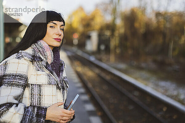 Schöne Frau mit Mobiltelefon wartet am Bahnhof auf den Zug