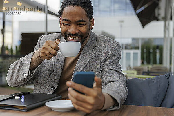 Glücklicher Geschäftsmann  der Kaffee trinkt und sein Smartphone benutzt