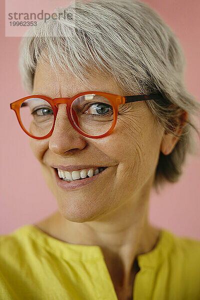 Lächelnde Frau mit Brille vor rosa Hintergrund