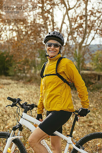 Glückliche Frau steht mit Mountainbike neben Bäumen im Wald