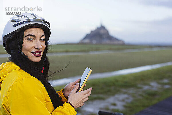 Lächelnde Frau mit Fahrradhelm und Smartphone