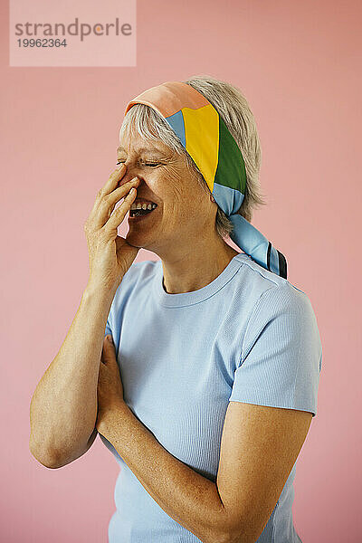 Frau bedeckt den Mund und lacht vor rosa Hintergrund