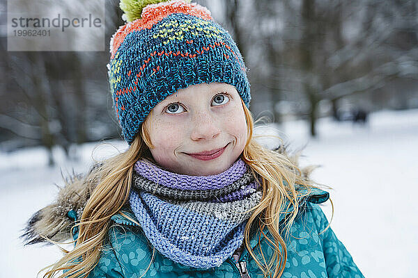 Lächelndes blondes Mädchen mit Schal und Strickmütze im Winter