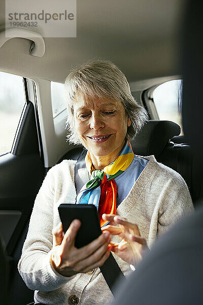 Lächelnde Frau sitzt im Auto und benutzt Smartphone