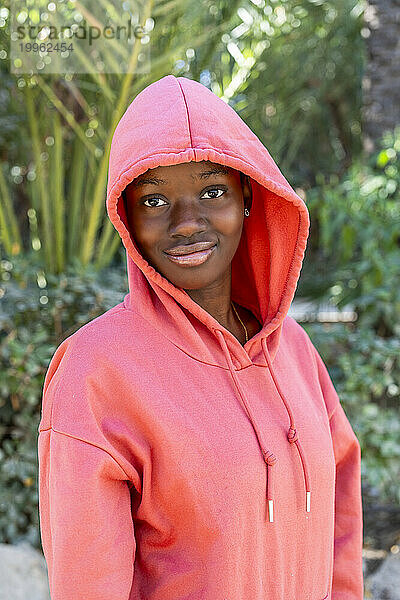 Lächelnde Frau trägt rosa Kapuzenshirt im Park