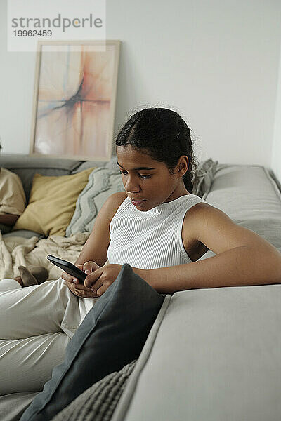 Vorpubertäres Mädchen sitzt zu Hause auf dem Sofa und benutzt Smartphone