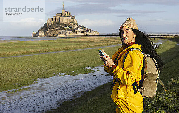 Frau mit Smartphone und Rucksack steht am Schloss Saint Michel