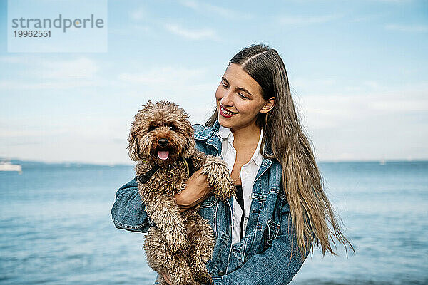 Lächelnde Frau mit Pudelhund vor dem Meer