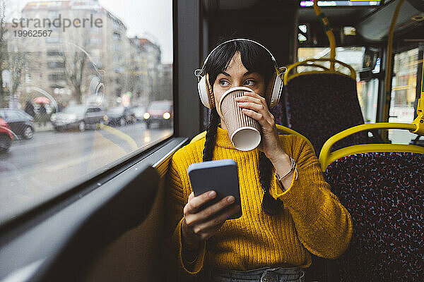 Frau trägt kabellose Kopfhörer und trinkt Kaffee im Bus