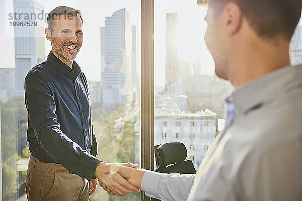 Glücklicher Geschäftsmann schüttelt seinem Kollegen im Büro die Hand