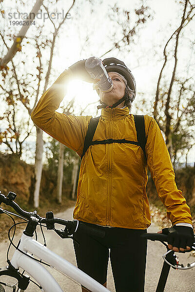 Frau trinkt Wasser aus Flasche in der Nähe von Mountainbike im Wald