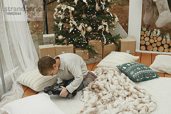Junge spielt mit Spielzeugauto auf Teppich neben Weihnachtsbaum zu Hause