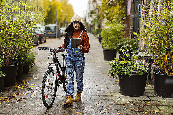 Frau benutzt Tablet-PC und läuft mit Fahrrad auf Fußweg