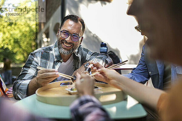 Freunde sitzen im Garten und haben Spaß beim Sushi-Essen mit Stäbchen