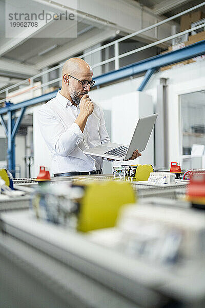 Geschäftsmann plant und nutzt Laptop in der Nähe von Maschinen in der Fabrik