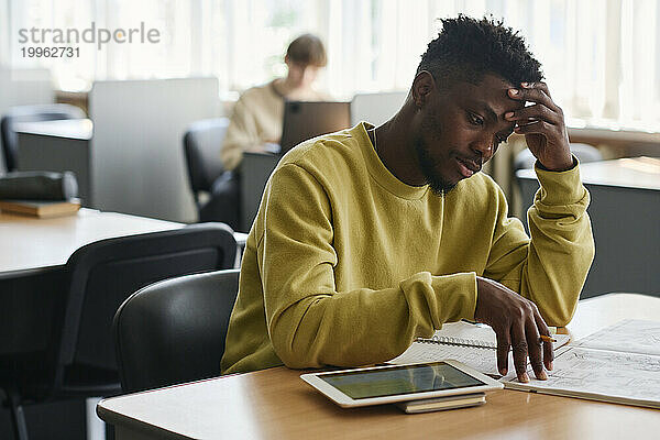 Müder Student lernt am Schreibtisch in der Bibliothek