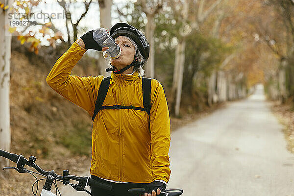 Frau steht mit Mountainbike und Trinkwasser im Wald