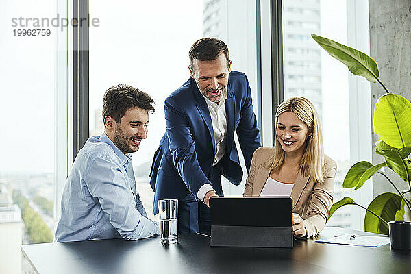 Lächelnder reifer Geschäftsmann erklärt Kollegen über Tablet-PC im Büro