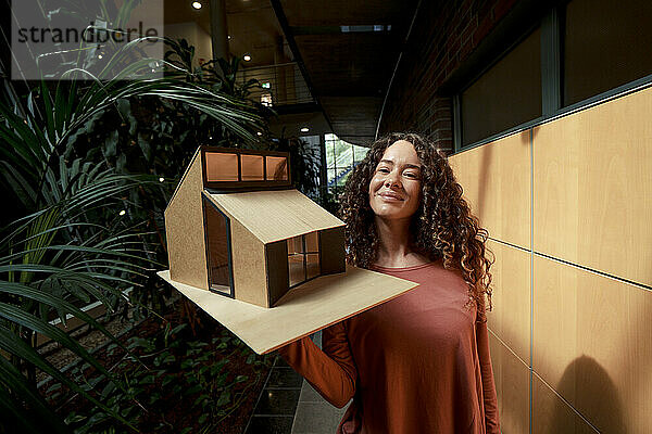 Lächelnder junger Architekt mit Musterhaus im Büro