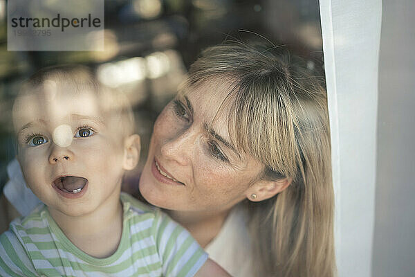 Netter Junge mit Mutter hinter transparentem Glasfenster