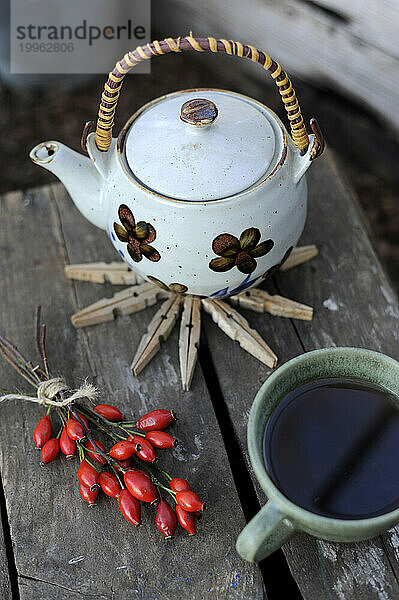 Rose hips  mug of tea and teapot standing on coaster made of clothespins