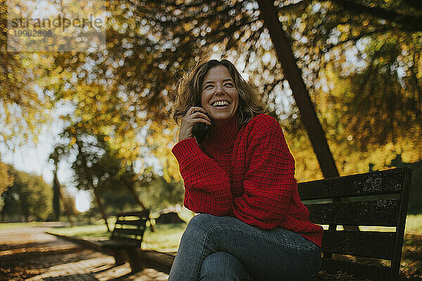 Glückliche Frau sitzt und lacht auf einer Bank im Herbstpark