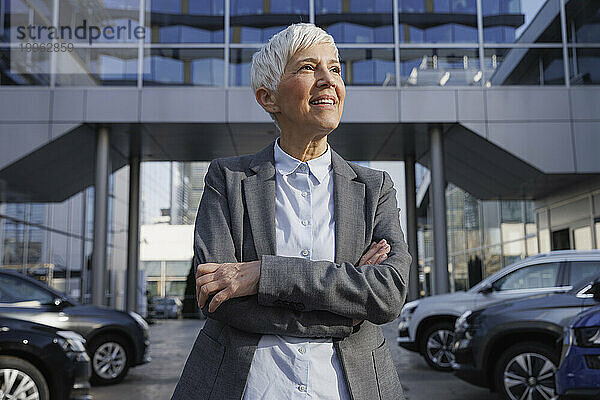 Nachdenkliche Geschäftsfrau steht mit verschränkten Armen vor dem Bürogebäude