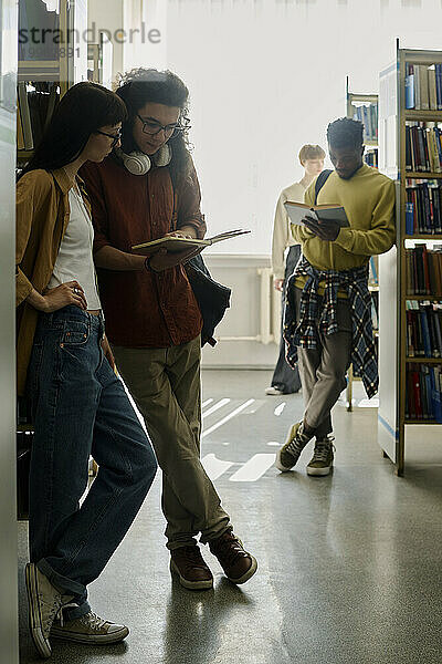 Studenten stehen neben Regalen und lesen Bücher in der Bibliothek