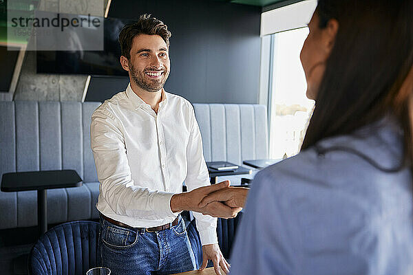 Lächelnder Geschäftsmann schüttelt einem Kollegen im Büro die Hand