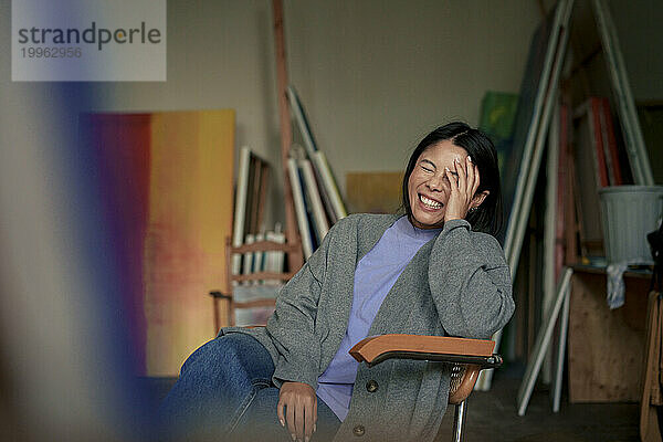 Glücklicher Maler mit geschlossenen Augen sitzt auf einem Stuhl im Kunstatelier